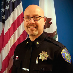 Assistant Police Chief John Murray's headshot in uniform in front of the US and California flags