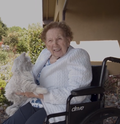 A senior woman is smiling while sitting a robotic white dog sits in her lap.