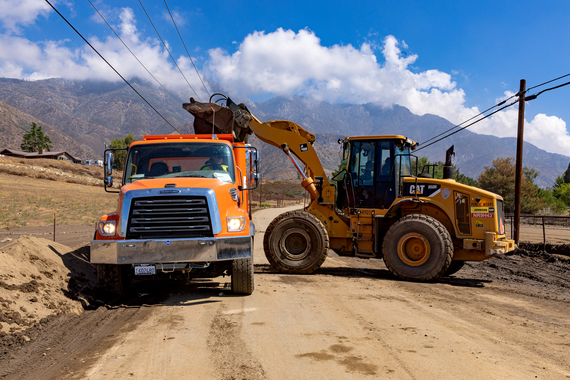 A photo of truck and backhoe clearing a dirt road after a storm.