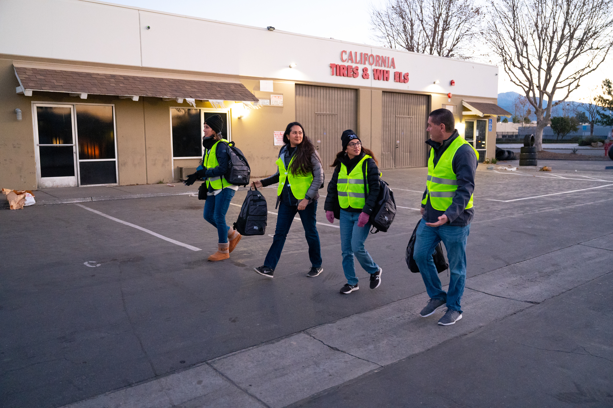 A group of four volunteers seen walking side-by-side in a street with a business store seen in the background.