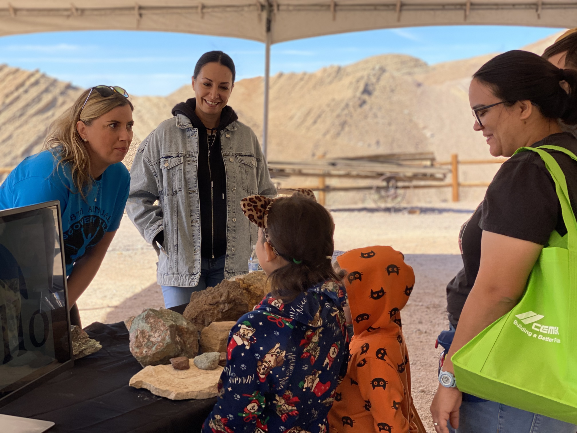A photo of two female representatives from Apollo Silver Mining are seen talking to children and adults with rock samples on a table.
