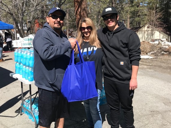 A family stands outside smiling holding a bag on a snowy mountain driveway with popup tents and a table of provisions in the background.