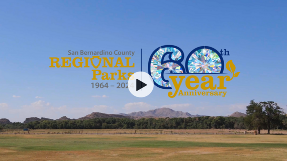 An photo with a video play button of Mojave Narrows Regional Park grass with mountains in the background in Victorville, California.