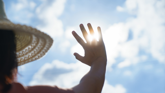 A photo of a woman wearing a hat looking up at the sky and sun.