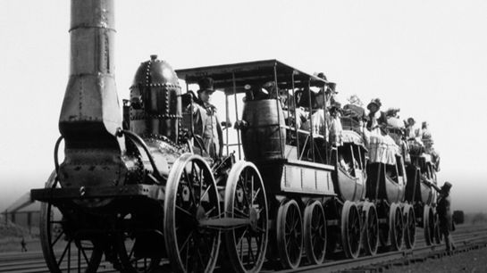 A photograph of an early steam-powered locomotive pulling several open carriages with passengers .