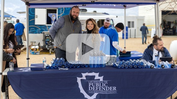 Several individuals stand behind a booth for the Law Offices of the SB County Public Defender as they give out blue water bottles.