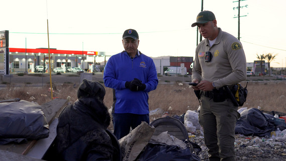 San Bernardino County Sheriff and man in blue jacket speak with homeless person outside, showing community outreach and public service efforts