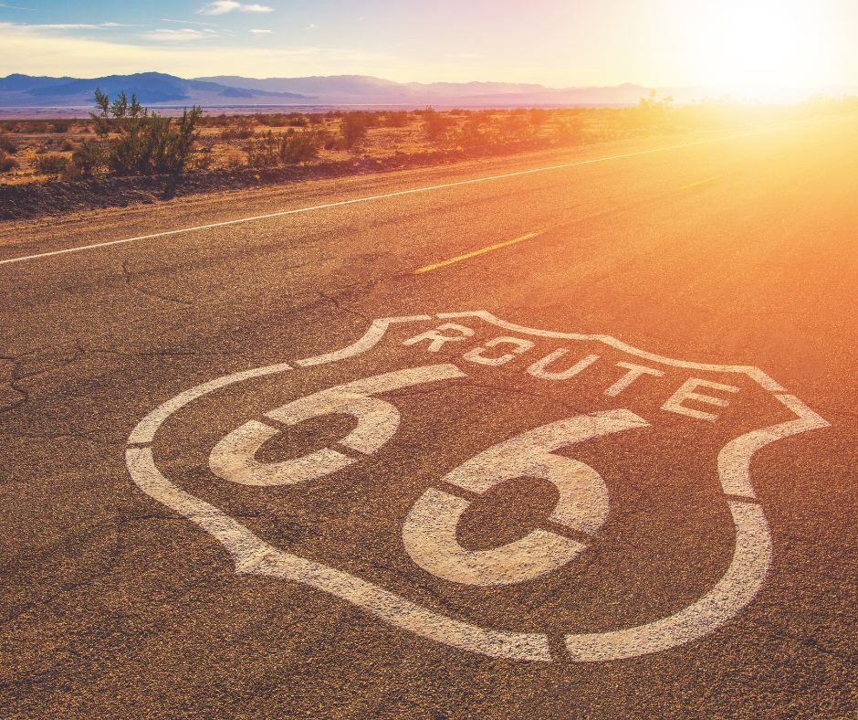 A portion of the Route 66 highway runs through the desert at sunset with the Route 66 logo emblazoned across it.