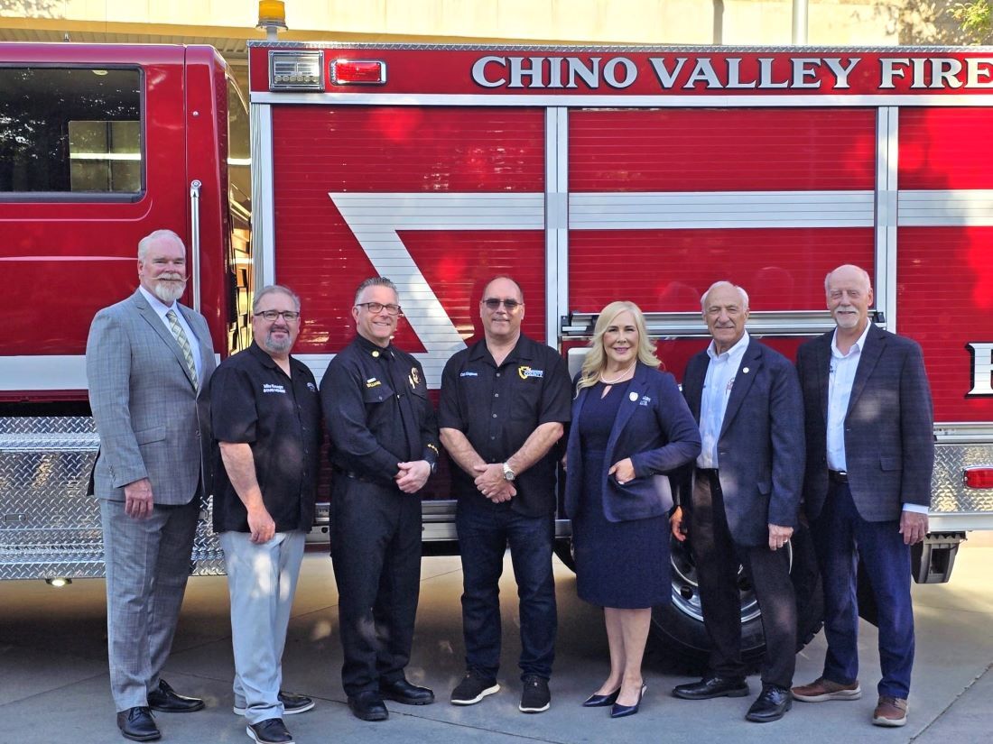Seven adults, including firefighters and officials, smiling in front of a red Chino Valley Fire truck.