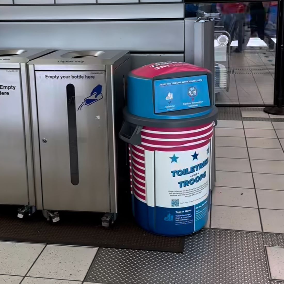Travelers line up at airport security near a donation bin for unused toiletries and a bottle station.