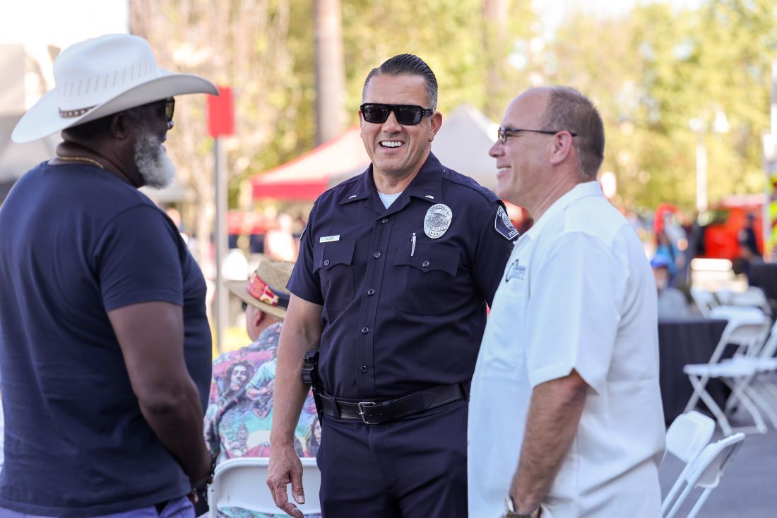 An Ontario police officer smiles while talking with two men at an outdoor community event.