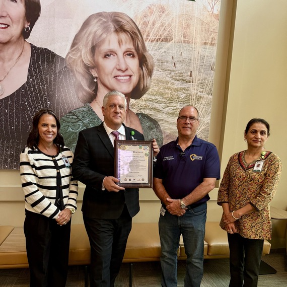 Supervisor Curt Hagman presents a framed certificate to hospital staff in front of a portrait wall.