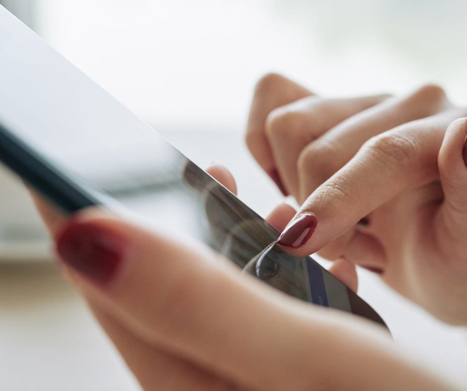 A hand with bright red nails touches a cell phone, presumably using apps.