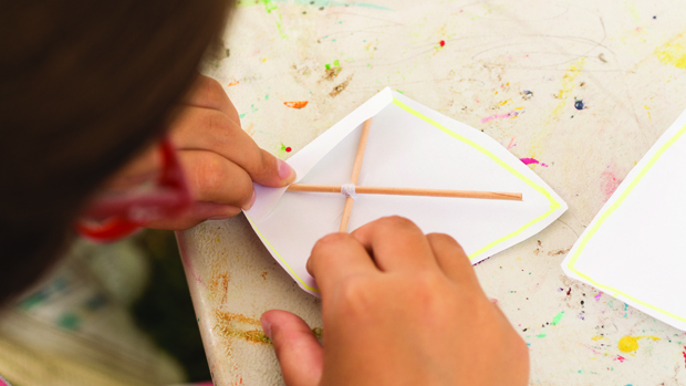A child making a small paper kite with wooden sticks.