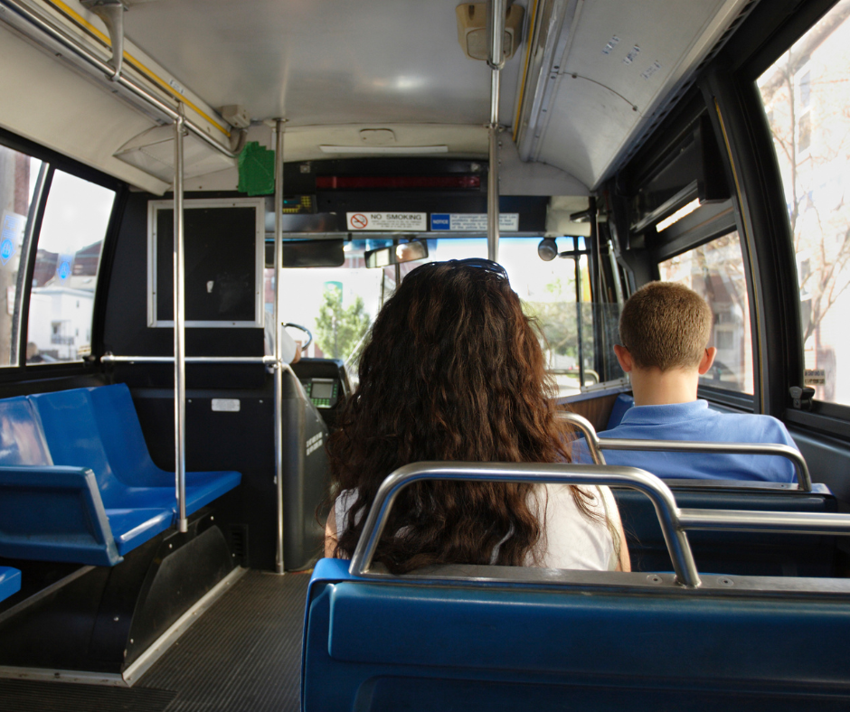 Two students--one male, one female--riding on a bus. They are both facing away from the camera.