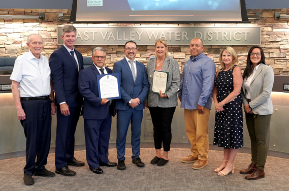 Eight people pose together indoors at East Valley Water District, with two individuals holding certificates of recognition