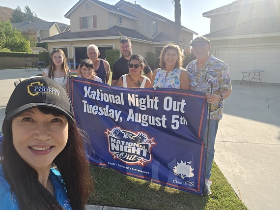 San Bernardino County staff and neighbors smile with a National Night Out banner in Chino Hills driveway.
