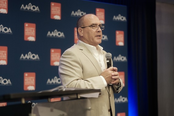 A male speaking on stage at the 2025 Asian American Hotel Association Conference.