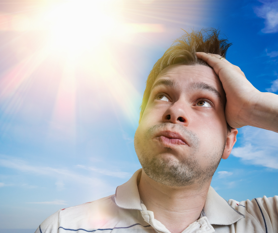 A man in a white and blue striped shirt with an overwhelmed look on his face stands under a blazing hot sun