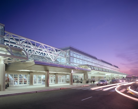 Ontario International Airport terminal lit at dusk with cars passing by.