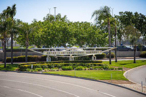 Ontario International Airport entrance sign surrounded by palm trees and greenery.