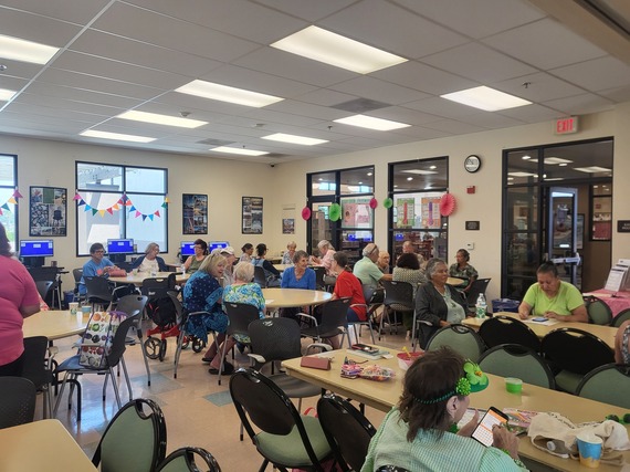 A lively senior center with tables and chairs filled with people socializing.