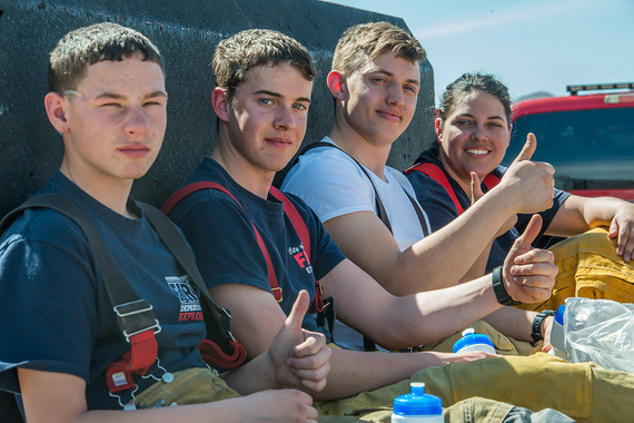 Four young San Bernardino County Fire Explorers sit beside fire equipment, while wearing some firefighting gear