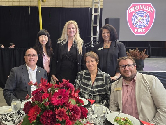 A group of six attendees smiling at a banquet table with red floral centerpiece at the Chino Valley Fire District event.