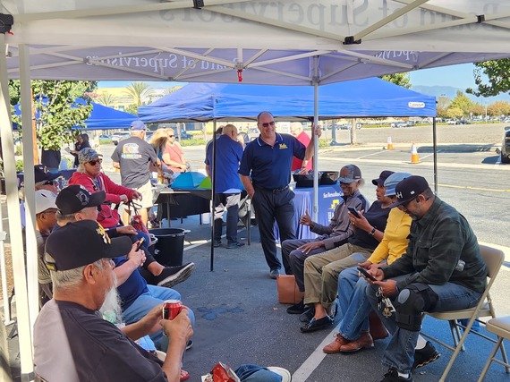 Veterans sitting under event canopies talking and relaxing while staff assist nearby at an outdoor resource event.