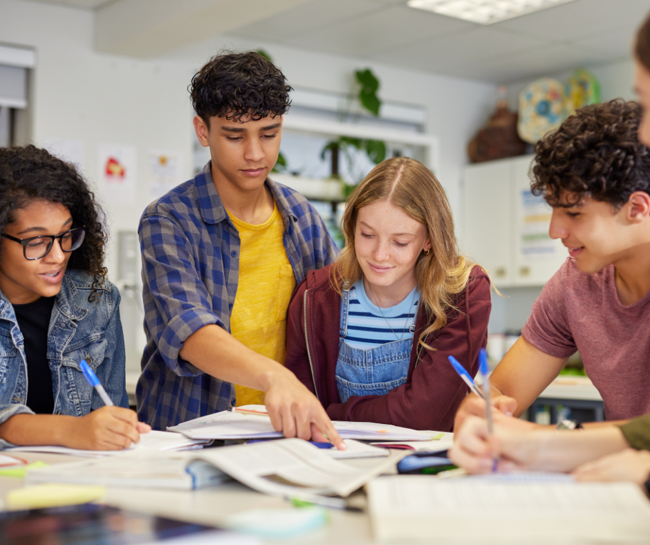 High school students looking at work on a desk while one student points at the current problem being solved.