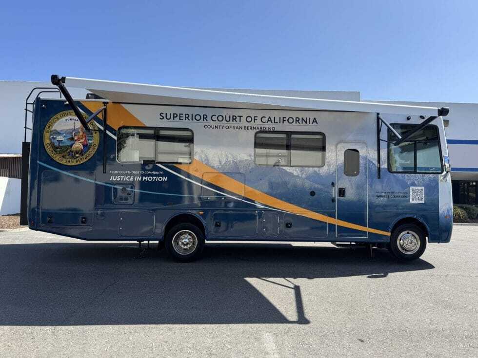 A large blue and gray mobile services vehicle labeled “Superior Court of California, County of San Bernardino” is parked outdoors. 