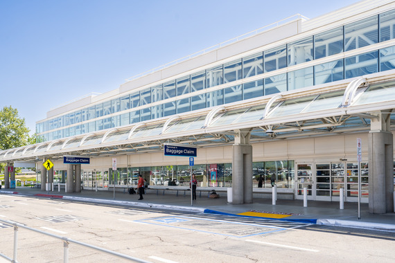 The front of Ontario International Airport Terminal 4 with baggage claim signs and travelers outside the entrance.