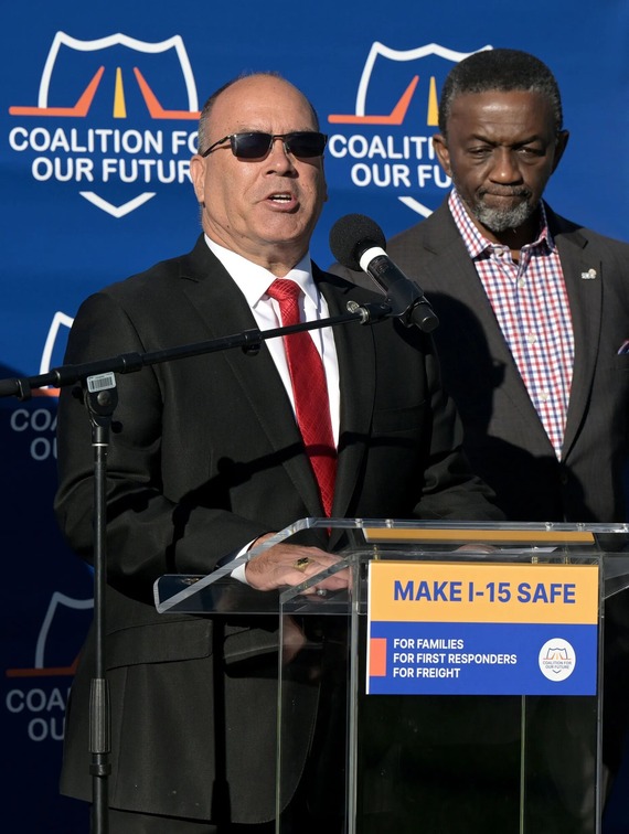 Man speaking at podium reading “Make I-15 Safe” during transportation safety press conference.