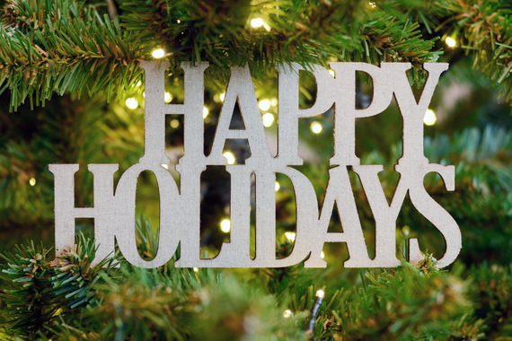 “Happy Holidays” ornament hanging on a decorated Christmas tree with lights.