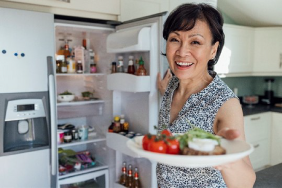 A woman stands by an open refrigerator holding a plate of nutritious food. 