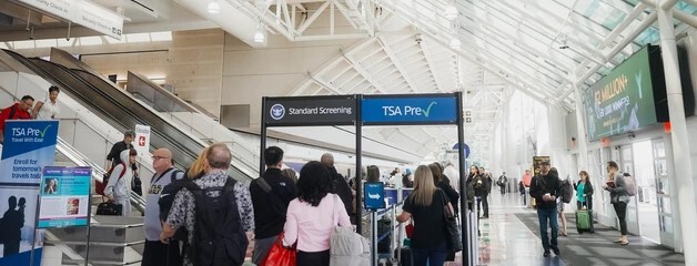 Passengers queue at airport security under TSA PreCheck and Standard Screening signs.