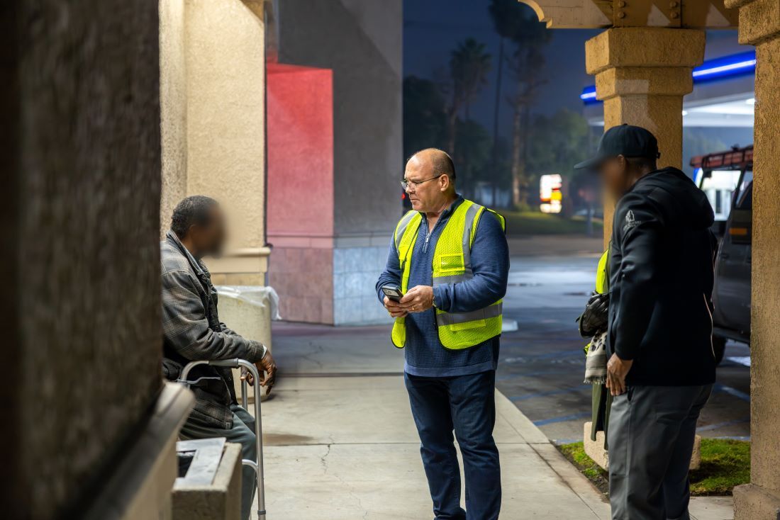 Supervisor Curt Hagman in a fluorescent vest conducting a survey of a homeless man during the 2026 Point-In-Time Count. 