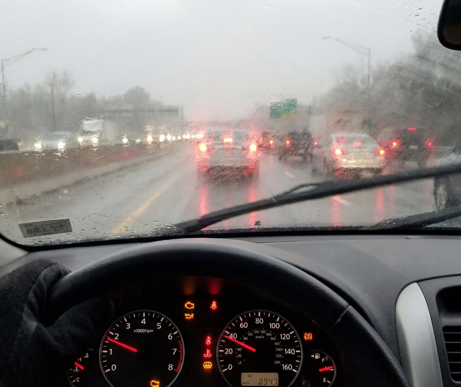 A rain soaked Southern California freeway packed with cars, as seen through the interior of a car, through the windshield on the drivers side