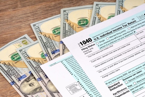 An image of dollar bills and U.S. Individual Income Tax Return 1040 forms lying on a wooden table.