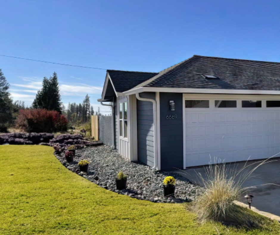 A suburban home with a gray exterior featuring decorative rock landscaping with fire-resistant landscaping design under a clear blue sky.