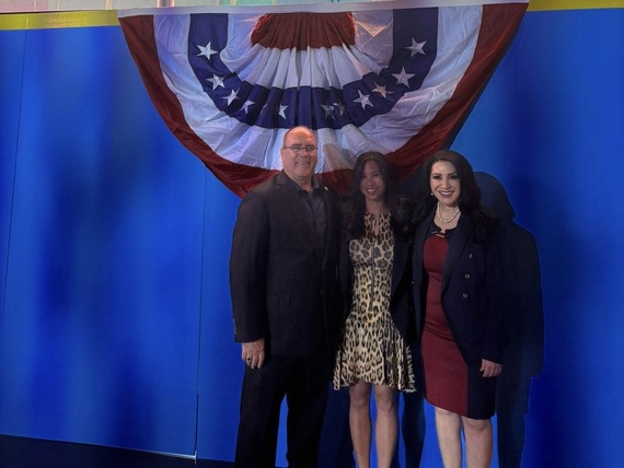 Supervisor Curt Hagman poses with two women under a patriotic display at indoor event.