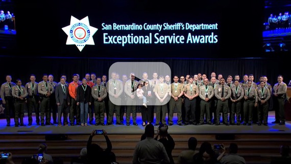 Medal-wearing deputies and individuals on stage at awards ceremony. Text: “San Bernardino County Sheriff’s Department Exceptional Service Awards”