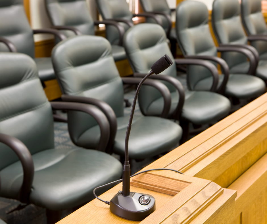 Empty seats covered in black vinyl sit in an empty jury box. A microphone is seen in the foreground.