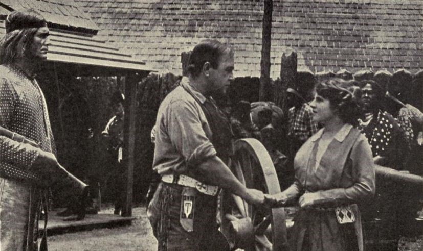 A scene from “The Call of the North” shows two people engaged in conversation while others observe.