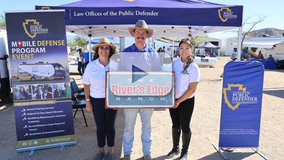 San Bernardino County "Law Offices of the Public Defender" canopy and three people holding "The River’s Edge Ranch” sign at mobile unit event.