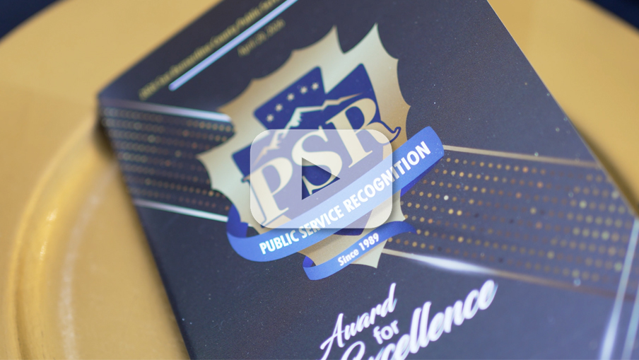 Program with text: PSR, PUBLIC SERVICE RECOGNITION, Since1989, & Award for Excellence” on a plate with video play button overlay.