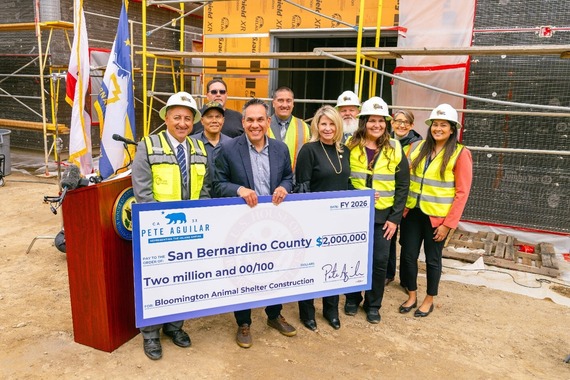 Smiling group in safety vests and helmets holds a $2M check at a construction site with scaffolding in the background.