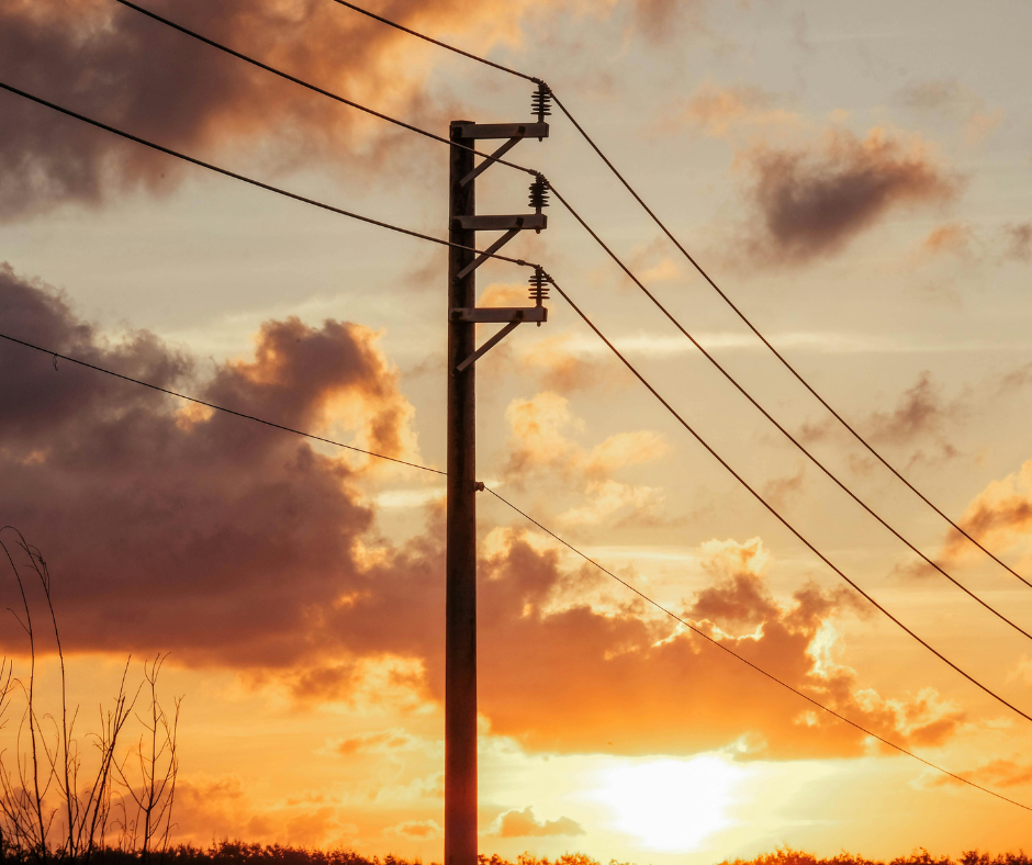 A power line with wires running in both directions sits in the foreground against a partly cloudy sunset