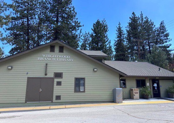 A small light green library building with "Wrightwood Branch Library" on the façade surrounded by tall pine trees.