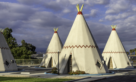Four cone structures that resemble teepees under a partly cloudy sky.